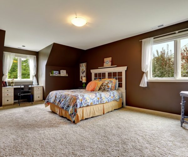 Spacious master bedroom interior with soft carpet floor and dark brown walls. Room has small office area by the window