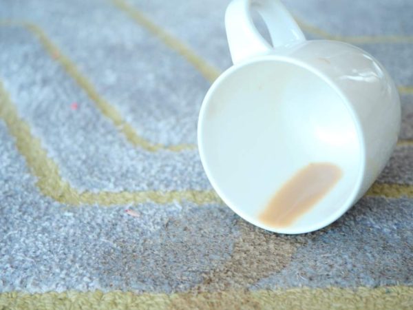 cup of coffee spilled on gray color carpet .