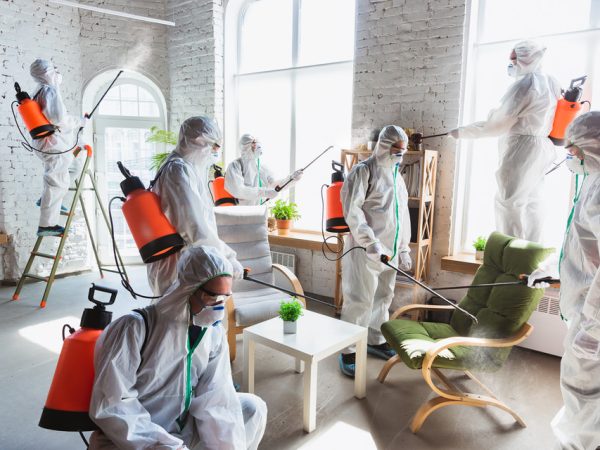 A disinfectors in a protective suit and mask sprays disinfectants in house
