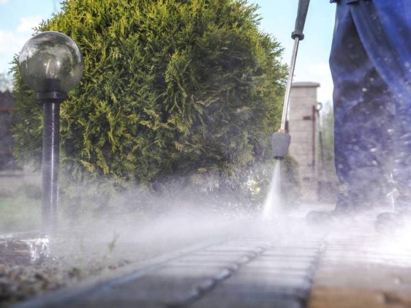 professional in blue pants pressure washing driveway